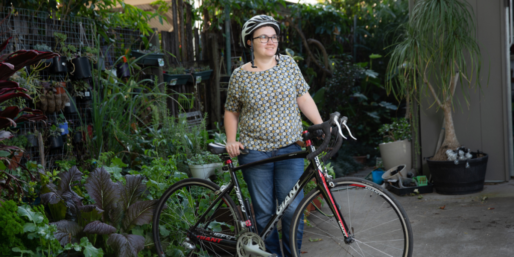 Woman with helmet on holding bicycle in her front courtyard