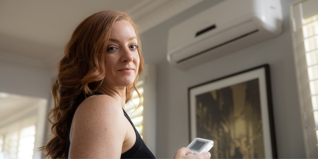 A woman (Marina Wood) standing looking into camera as she turns down aircon temperature at home.