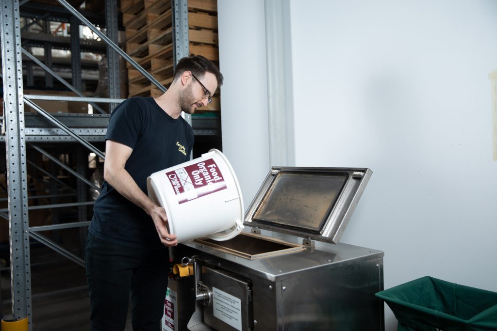 Cafe worker disposing of food waste into industrial composter.