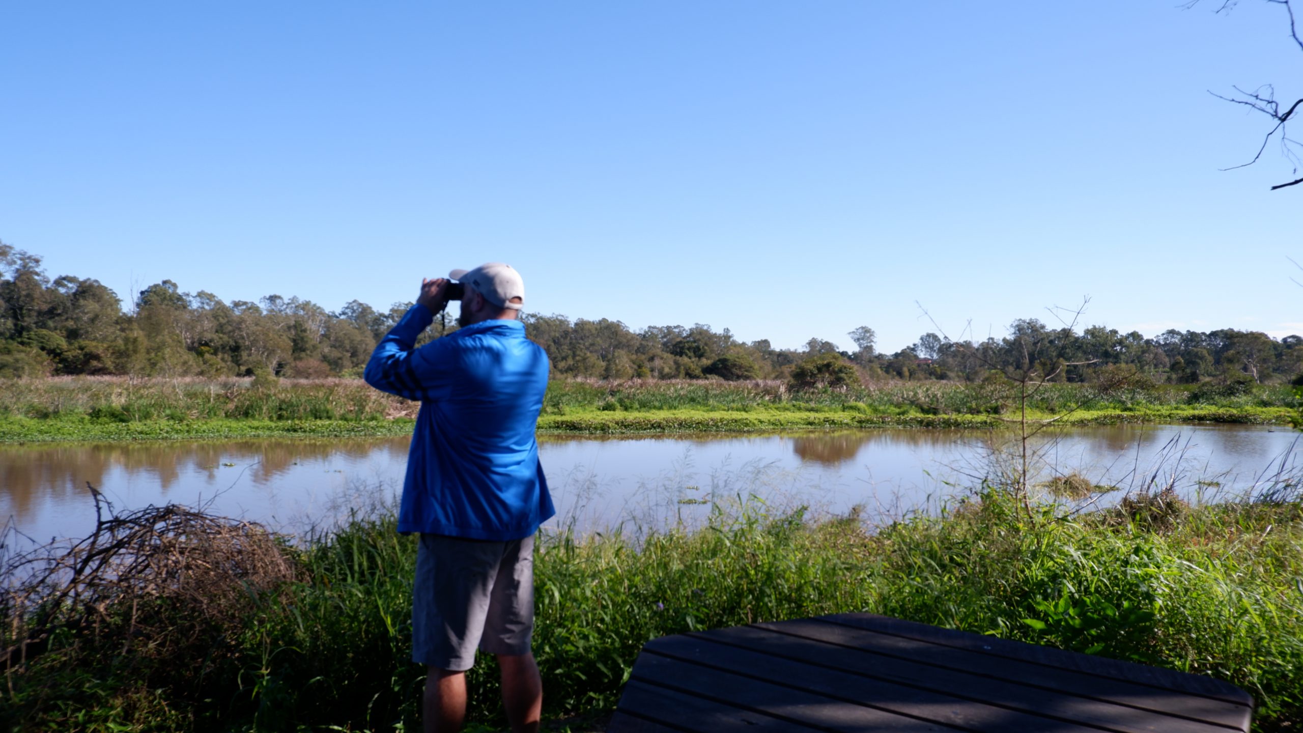 A man with binoculars looking at a creek