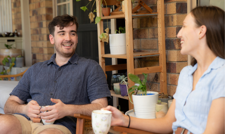 Housemates sitting on balcony looking at each other laughing while drinking coffee