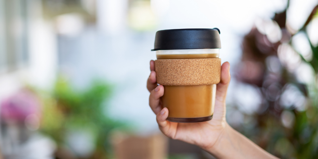 A person's hand holding a reusable coffee cup