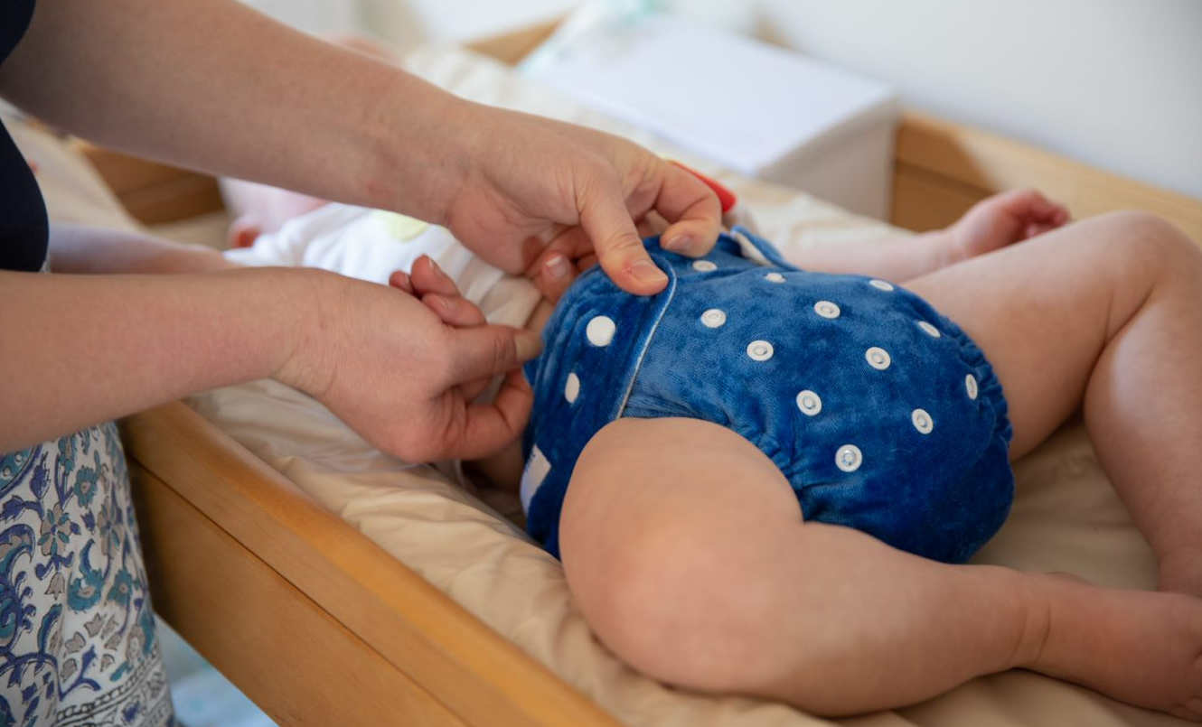 Image of mothers hands changing blue reusable nappy on baby.