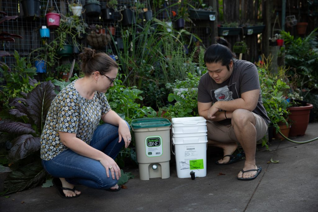 Two Brisbane residents in their backyard looking at their bokashi bin and compost caddy
