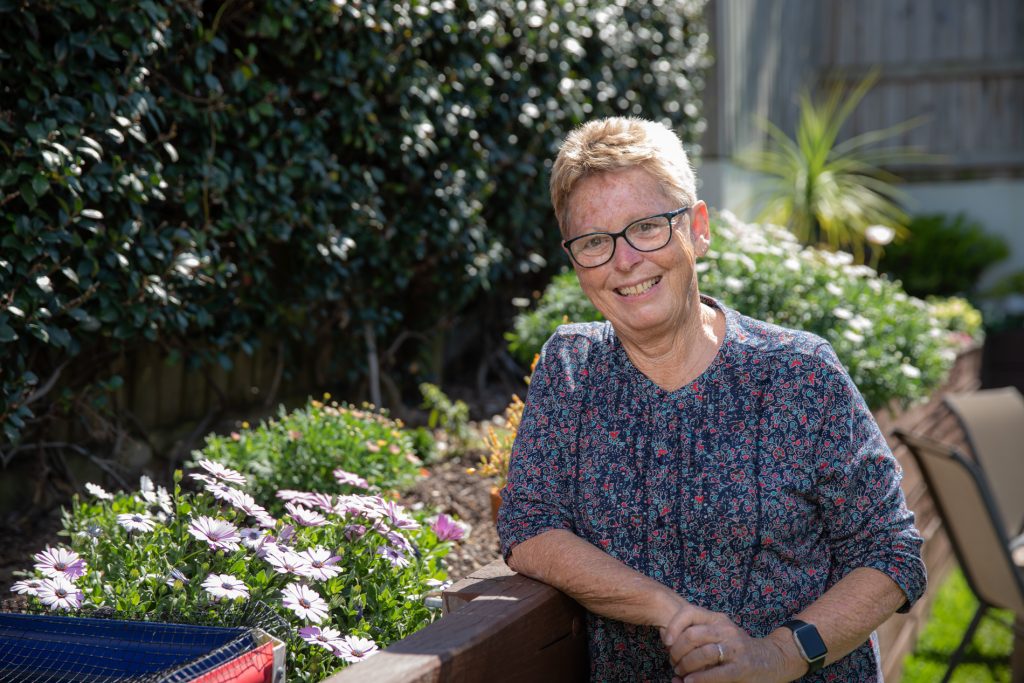 Vicki cleaning against her high-set flower and vegetable garden smiling into the camera.