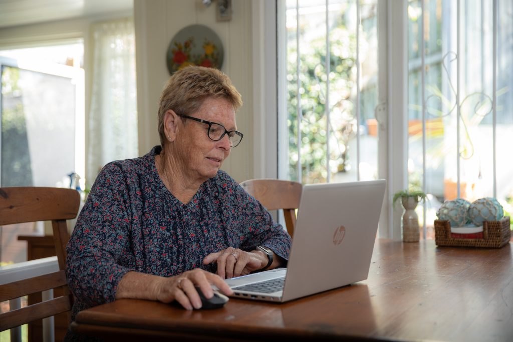 Vicki sitting at dining room table browsing on her laptop.