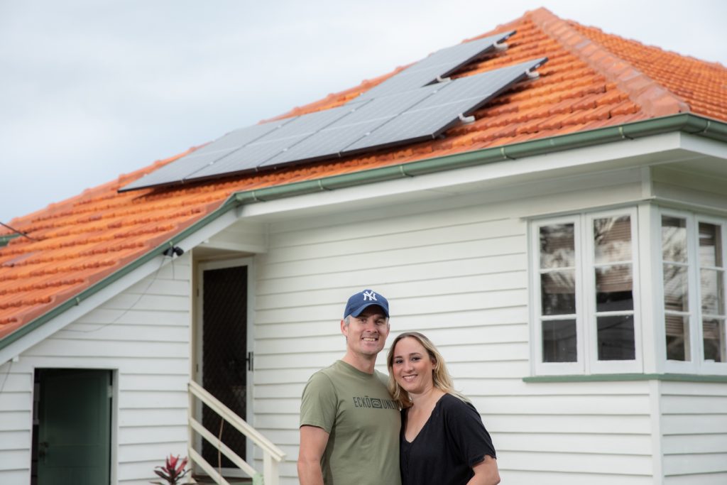 Brad and Karina standing in front of their house with solar panels visible on the roof.