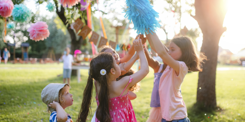 KIds at a party underneath tissue paper pom poms