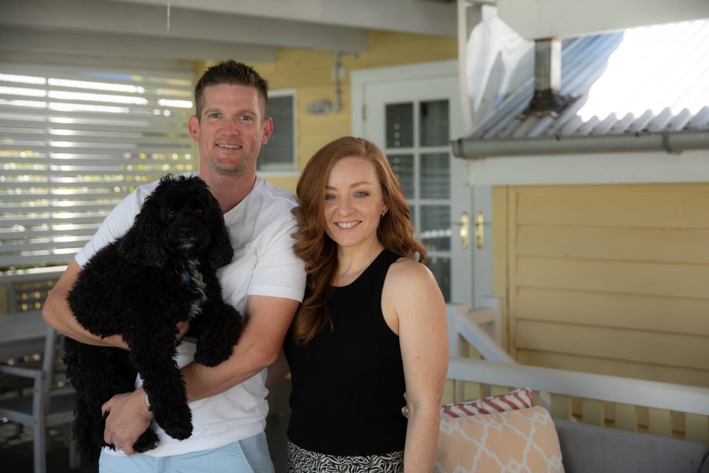 Marina and Adam Wood holding their dog, smiling into the camera