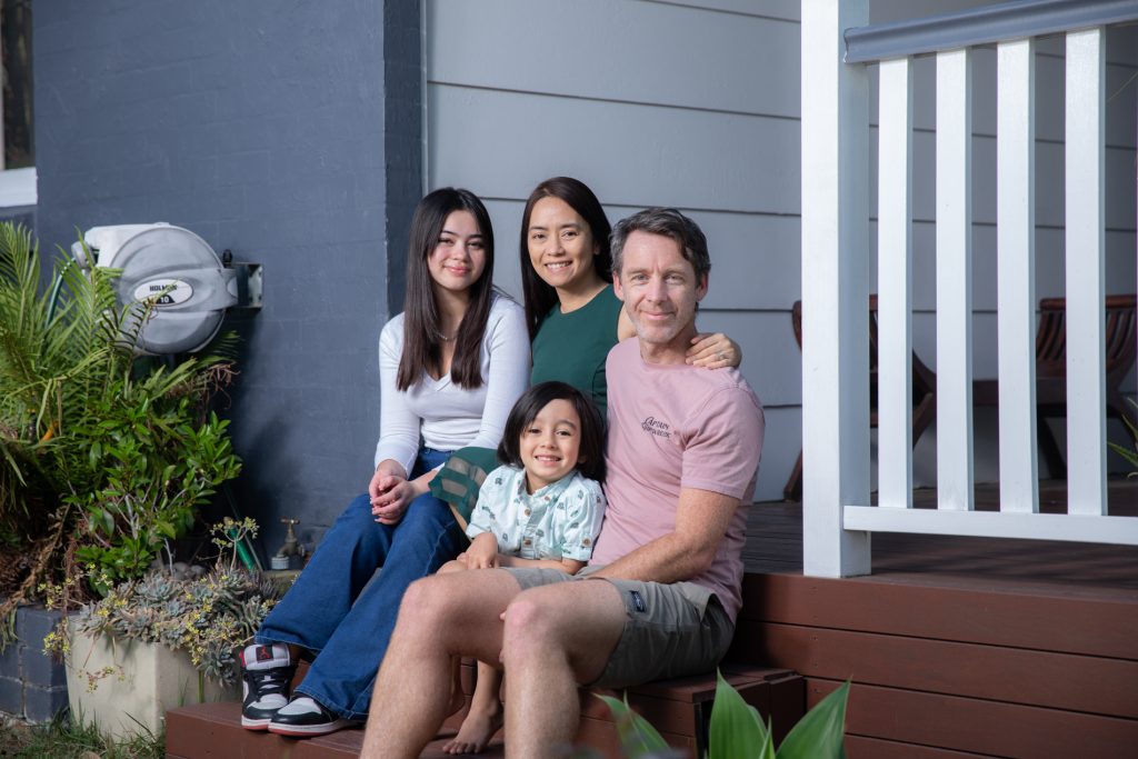 Declan and Verna sitting with their two children on the front porch stairs smiling into camera.