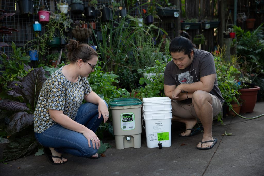 Miriam and Nicholas crouching next to a compost caddy and bokashi bin.