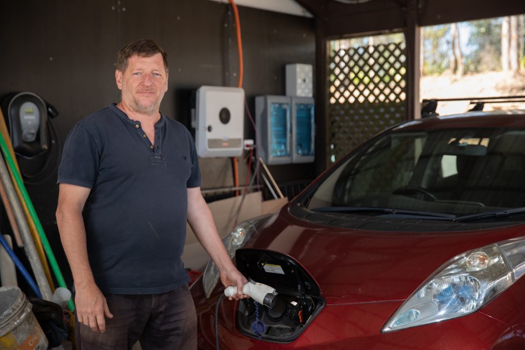 Ian Gittus standing infront of his electric car, charging it through the bonnet.