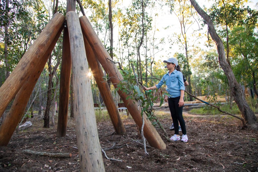 A girl using some sticks to build a bush cubby