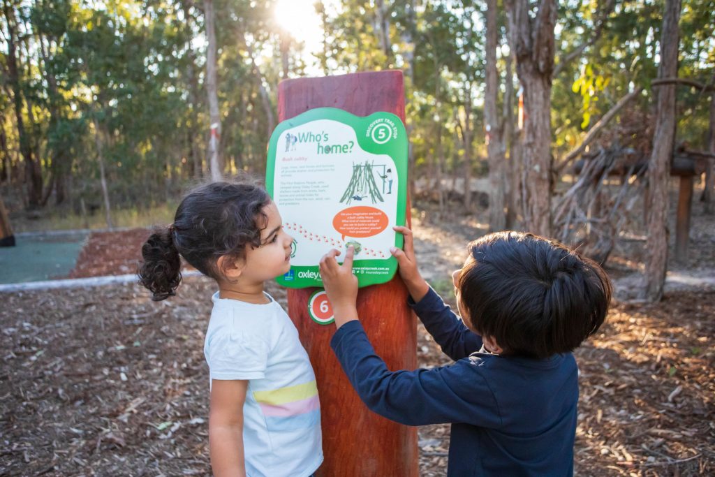 Kids pointing a to a sign on a tree