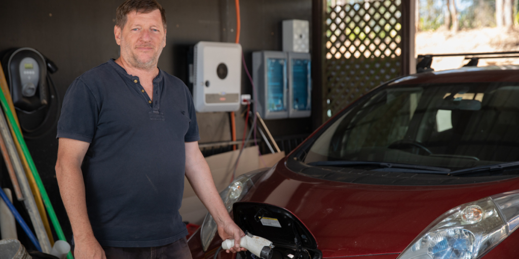 Ian Gittus standing infront of his electric car, charging it through the bonnet.