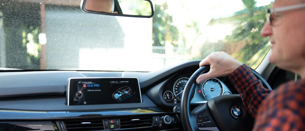 Over-the-shoulder shot of a driver in car with 'eco-mode' showing on the digital screen interface of the car.