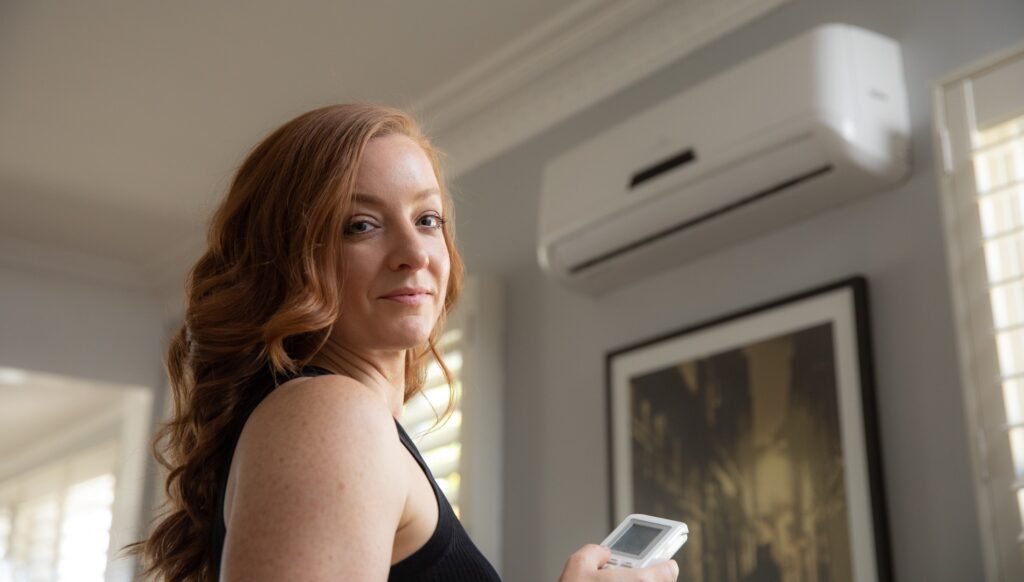 Woman smiling at camera while turning aircon off with remote.