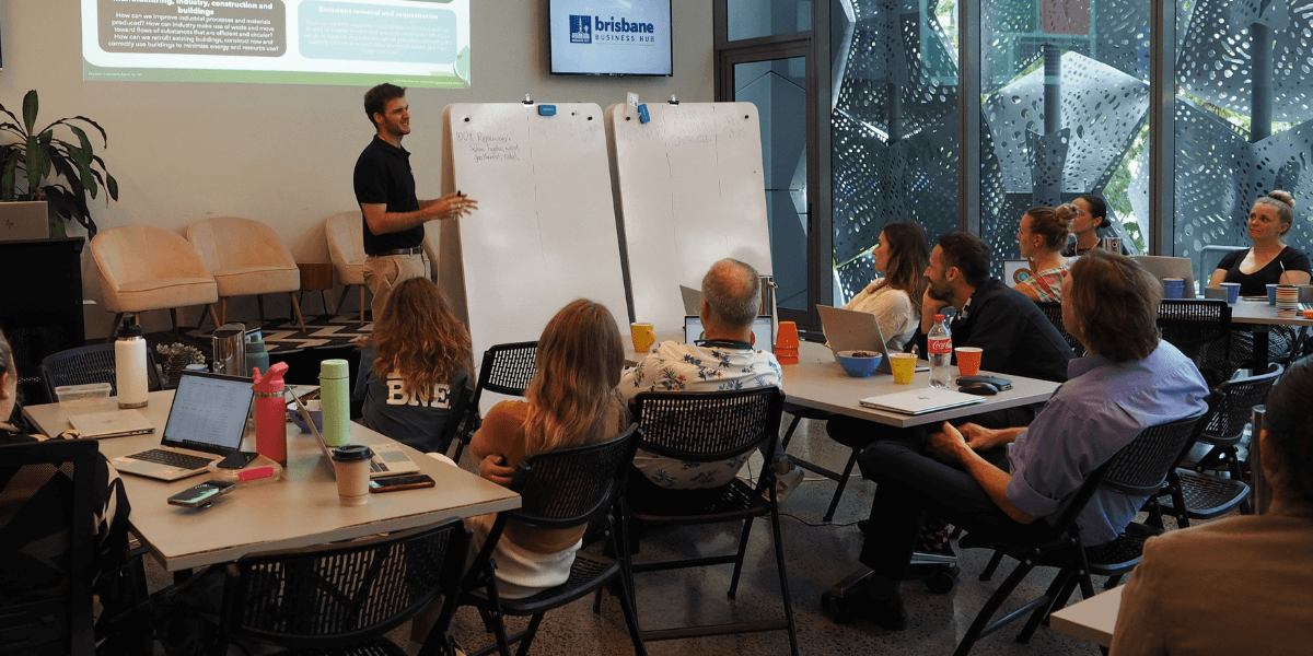 A group of BSA staff members watching a workshop being presented by a training facilitator who is talking to writing on a white board.